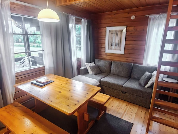 A cozy room with a wooden floor, a sofa, a table with a book, and a window with curtains. - Ukko 14 by Interhome (Kuusamo)