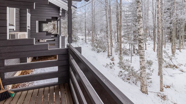 Una cabaña de madera con un balcón que da a un bosque nevado.