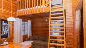 Un interior acogedor de cabaña con un dormitorio en entrepiso, una zona de comedor y un espacio de descanso.