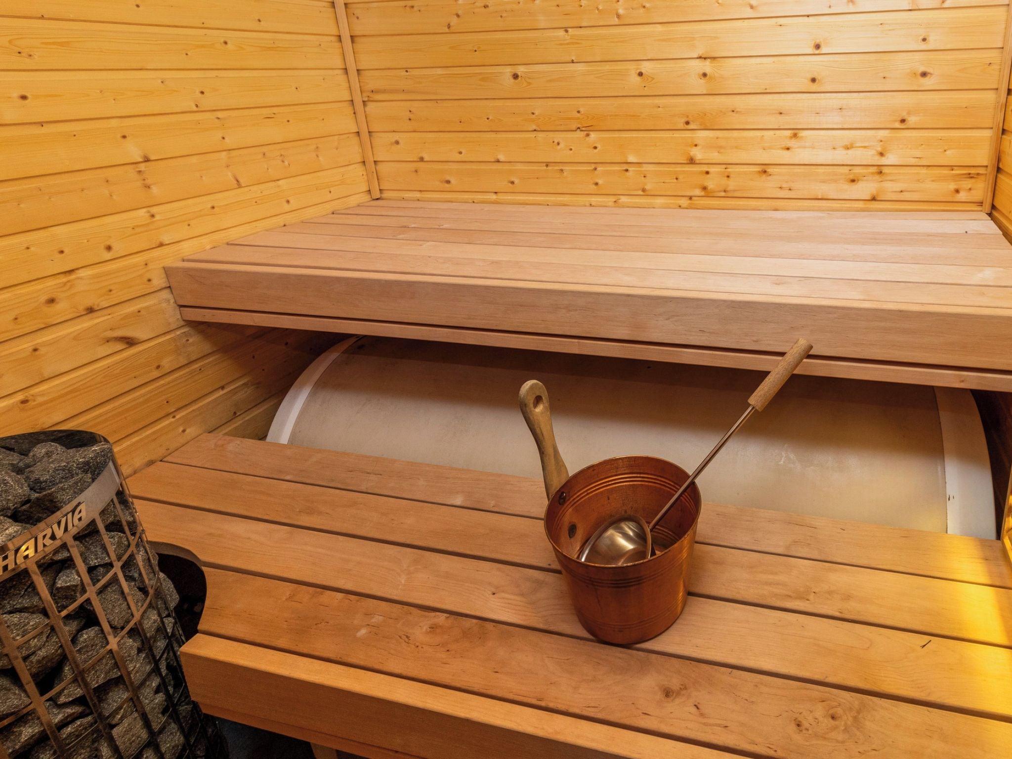 Un sauna con bancos de madera y un cubo de cobre con una cuchara.
