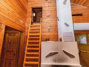 A wooden interior with a wooden staircase leading to a loft area, a stone fireplace, and a sign reading 'Lomarengas'.
