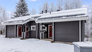 Un edificio de dos pisos con exterior oscuro y puertas rojas, rodeado de árboles cubiertos de nieve.