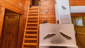Un interior de madera con una escalera de madera que conduce a una zona superior, una chimenea de piedra y una puerta con la etiqueta 'Lomarengas'.