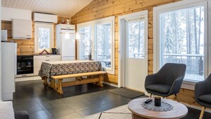 Interior acogedor de una cabaña con cocina, comedor y zona de estar junto a grandes ventanales.