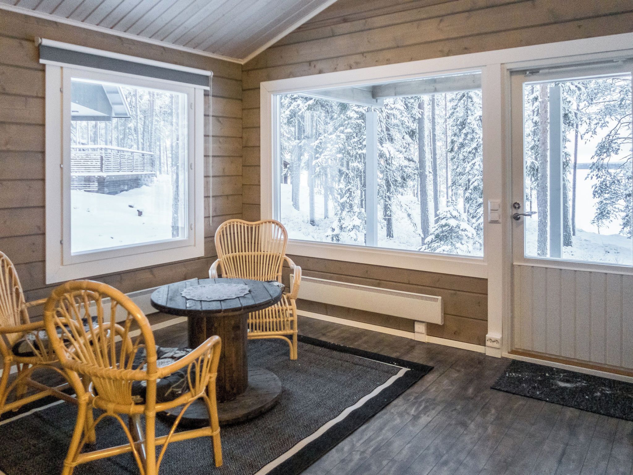 A room with a table and chairs, large windows with snowy views, and a radiator.