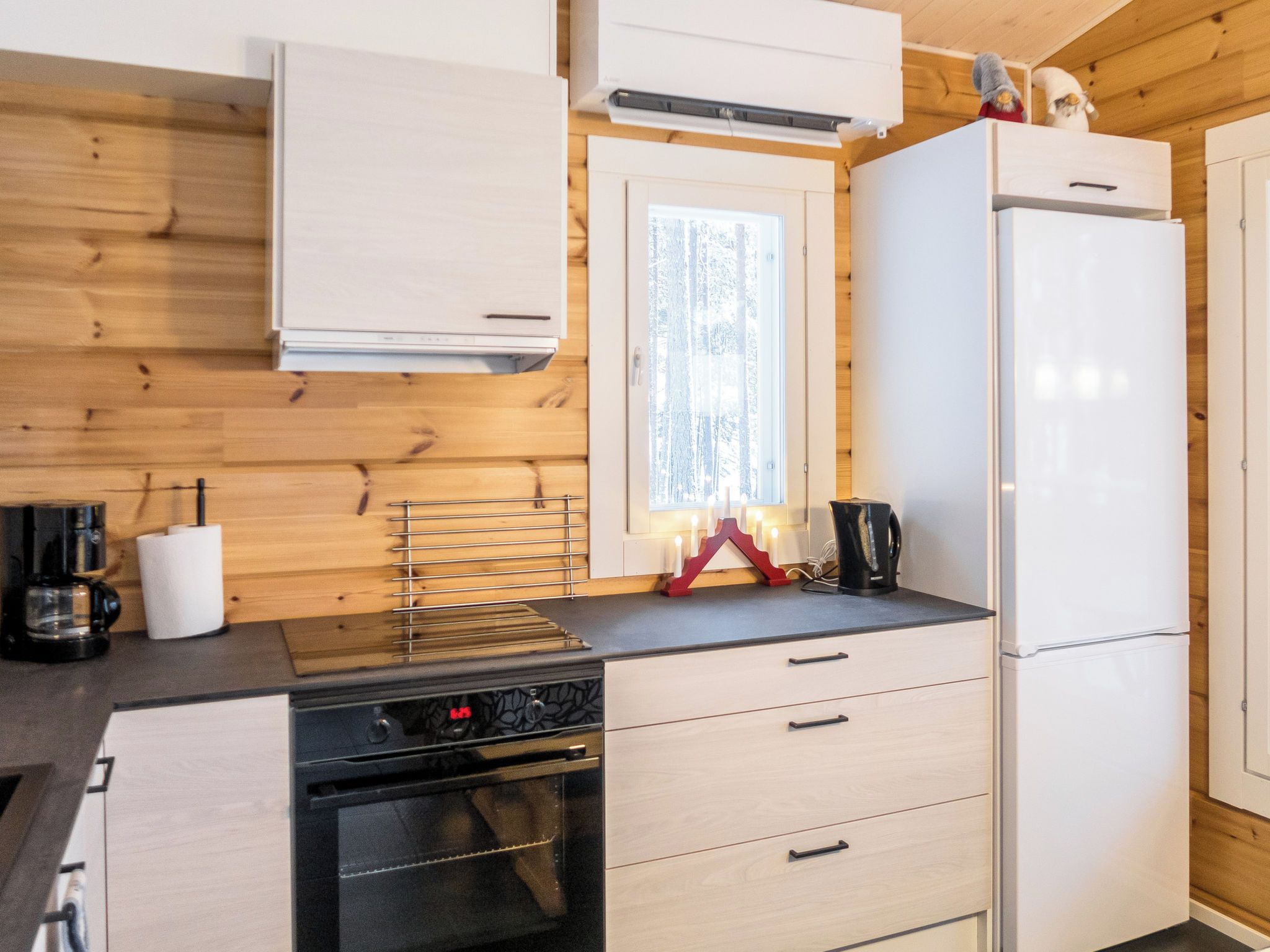 Une cuisine moderne avec des murs en bois, un fourneau, un réfrigérateur et une fenêtre donnant sur les arbres.