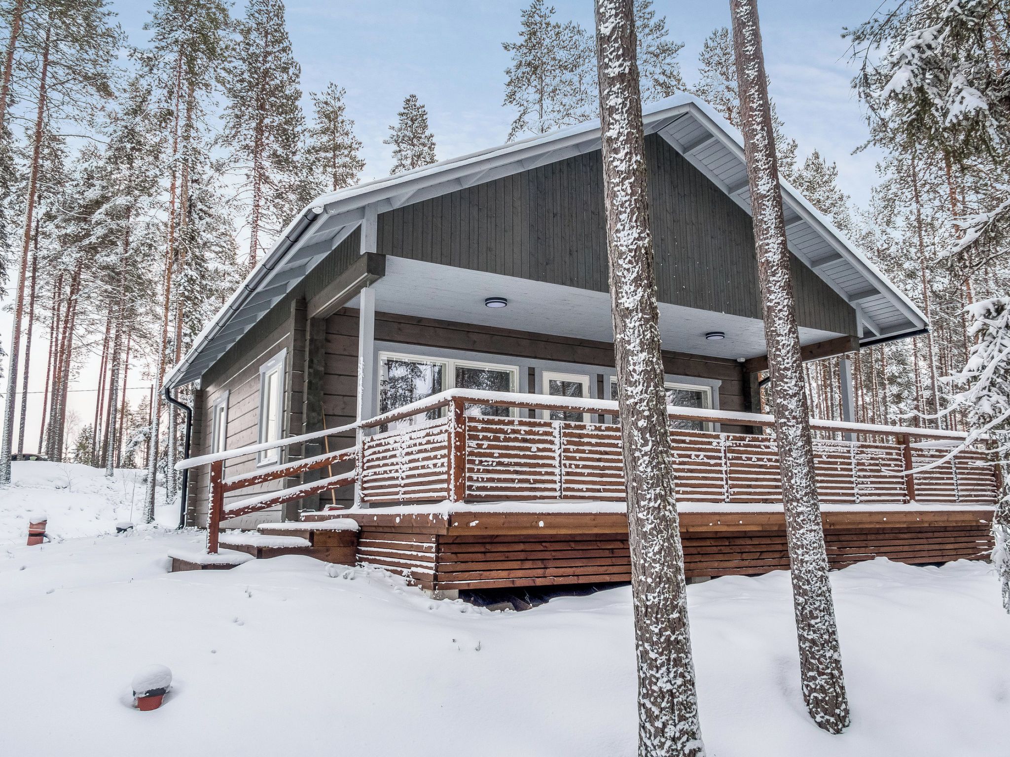 Une cabane au revêtement extérieur en bois, dotée d’un porche abrité et surplombant un paysage enneigé.