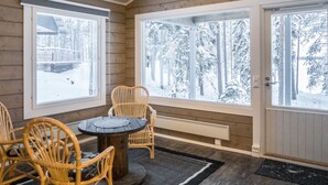 Una habitación acogedora con detalles de madera, ventanas amplias, una mesa redonda y sillas de mimbre.