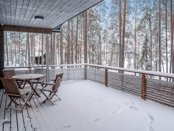 A covered outdoor area with a wooden deck, metal railing, and a table with chairs.