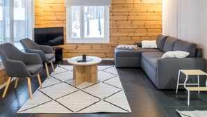 Una sala moderna con un sofá gris, dos sillones, una mesa de centro y un televisor.