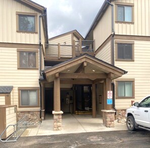 A multi-story building with a covered entrance, stone pillars, and a parking area with a white SUV. - Walk to Main St. • Near Snowflake Lift • Hot Tubs+Pool (Breckenridge)