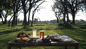 A picnic table set outdoors with food and drinks, surrounded by trees.