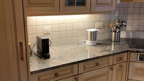 A kitchen with wooden cabinets, a granite countertop, a coffee maker, and a kettle. - Alpenglühn by Interhome (Adelboden)