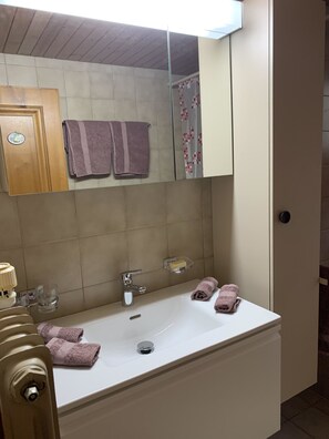 A bathroom with a white sink, two towels, a mirror, and a shower curtain. - Alpenglühn by Interhome (Adelboden)