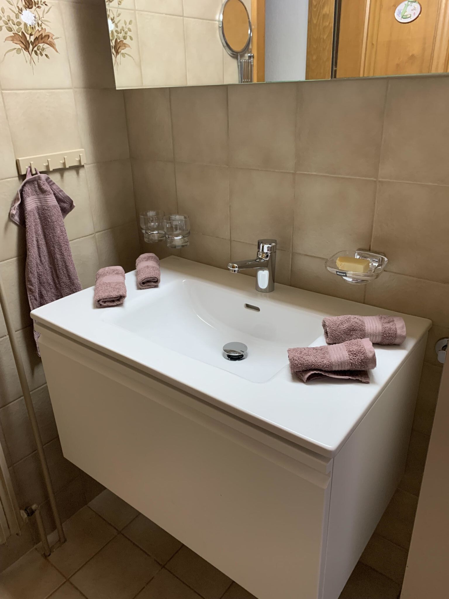 A bathroom with a white sink, a mirror, a towel rack, and a soap dish.