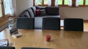 A cozy room with a wooden dining table, grey sofa, and a large window with curtains. - Alpenglühn by Interhome (Adelboden)