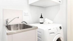 Une buanderie moderne équipée d’un évier en acier inoxydable, d’un lave-linge et d’une bouteille de lessive Glow Lab.