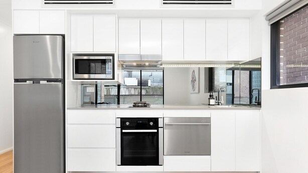 Une cuisine moderne avec des meubles blancs, un réfrigérateur en acier inoxydable, un four à micro-ondes, une cuisinière et un lave-vaisselle.