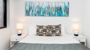 Ein modernes Schlafzimmer mit einem großen abstrakten Gemälde, zwei Nachttischlampen und Kissen mit Muster.