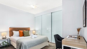 A modern hotel room with a large bed, bedside lamps, a wooden desk, and a chair.