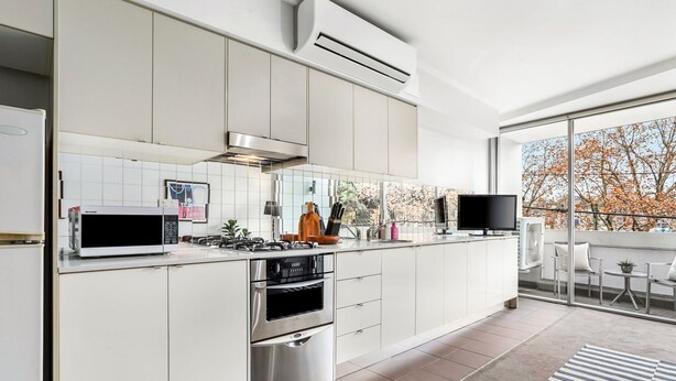 A modern kitchen with white cabinetry, stainless steel appliances, and a large window offering a view of trees.