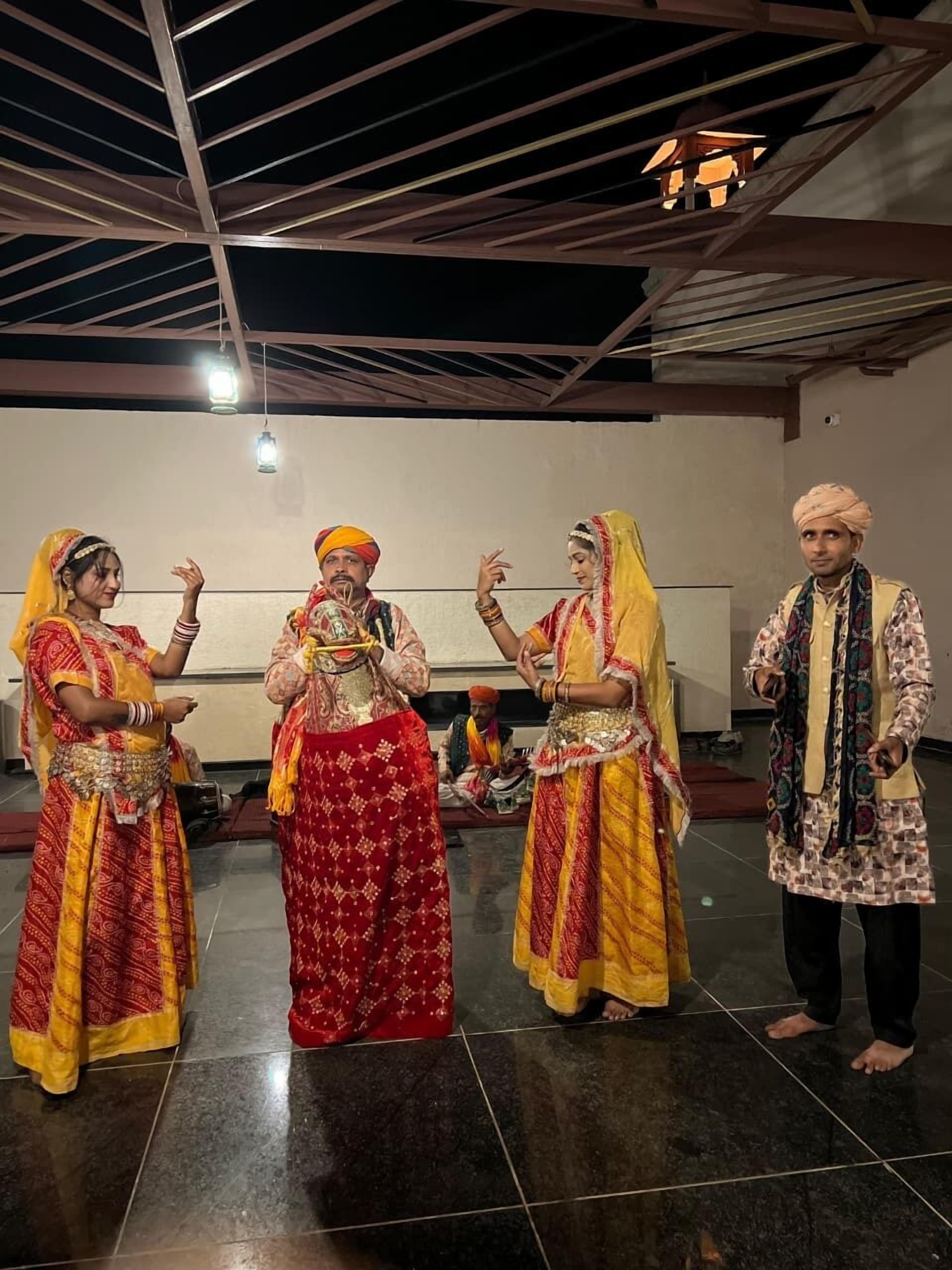 A group of people in traditional attire performing in a spacious indoor area with a high ceiling and tiled floor.