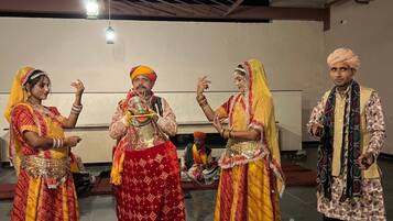 A group of people in traditional attire performing in a spacious indoor area with a high ceiling and tiled floor.