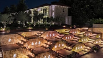 A multi-level stone staircase with integrated lighting, leading to a building with a stone facade and a balcony.