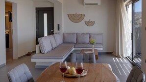 Ein modernes Wohnzimmer mit einer Eckcouch, einem Esstisch mit Weingläsern und einem großen Fenster mit Vorhängen.