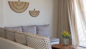 Ein modernes Wohnzimmer mit einer Couch, zwei gewebten Wandbehängen, einem Holztisch mit Blumenvase und einem Fenster mit durchsichtigen Vorhängen.