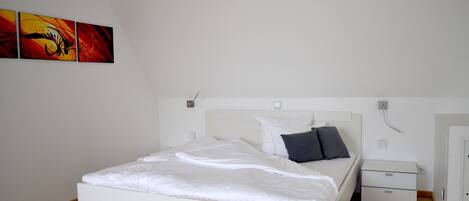 A bedroom with a white bed, a nightstand, a dresser, and three paintings on the wall.