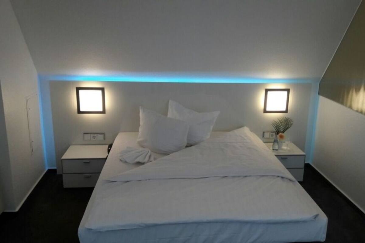 A modern hotel room with a large bed, two bedside tables, and a nightstand with a lamp.