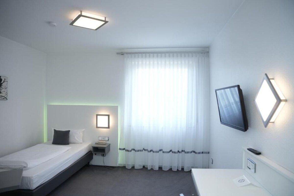 Une petite chambre propre, avec un lit, une table de chevet et un téléviseur fixé au mur.
