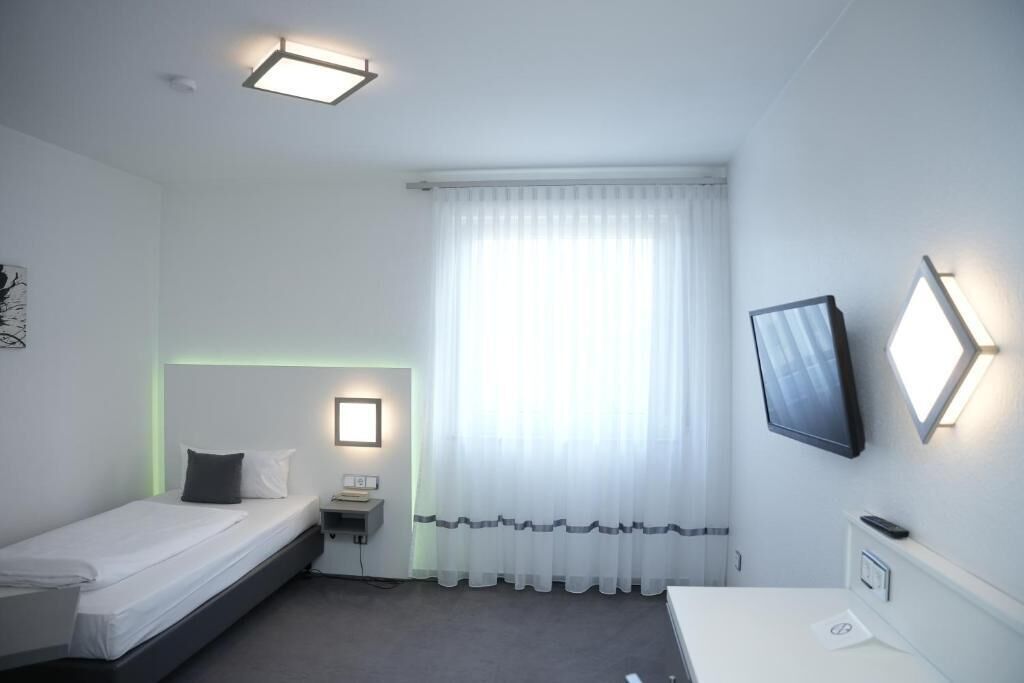 A small, clean room with a bed, bedside table, and a TV mounted on the wall.