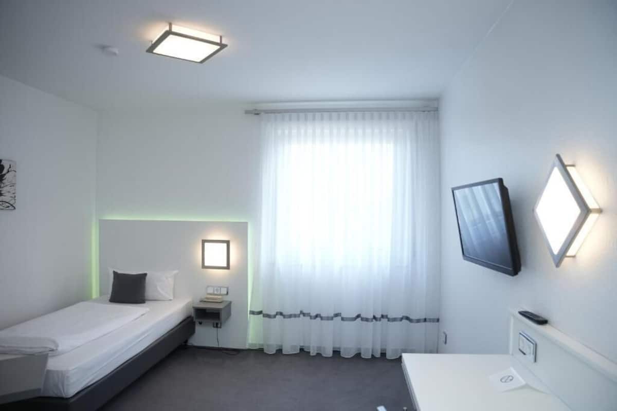 A small, clean room with a bed, bedside table, and a TV mounted on the wall.