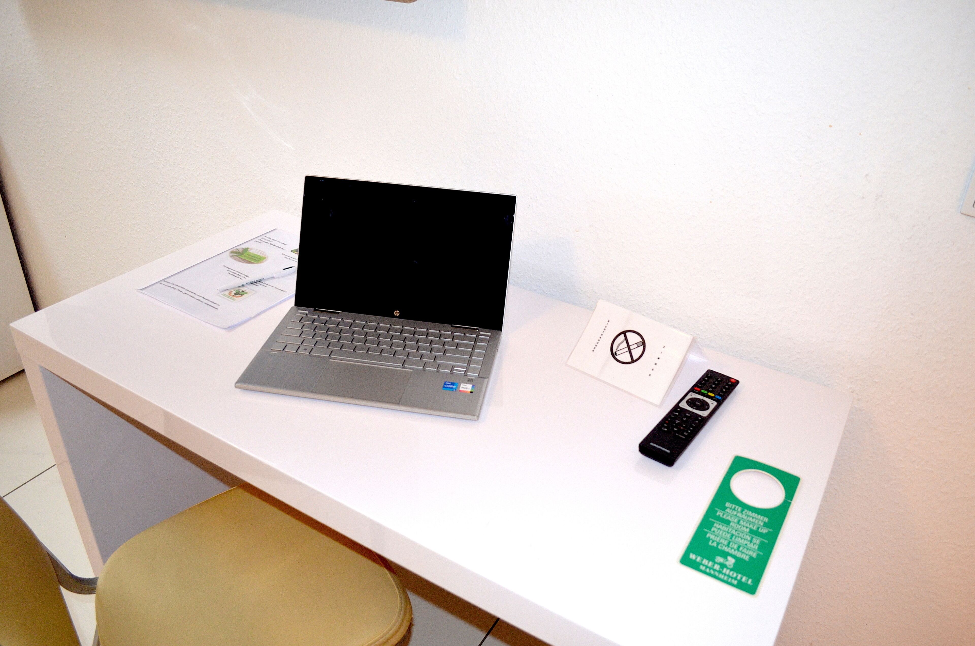 A laptop, a remote control, and a green hotel key card on a white desk.