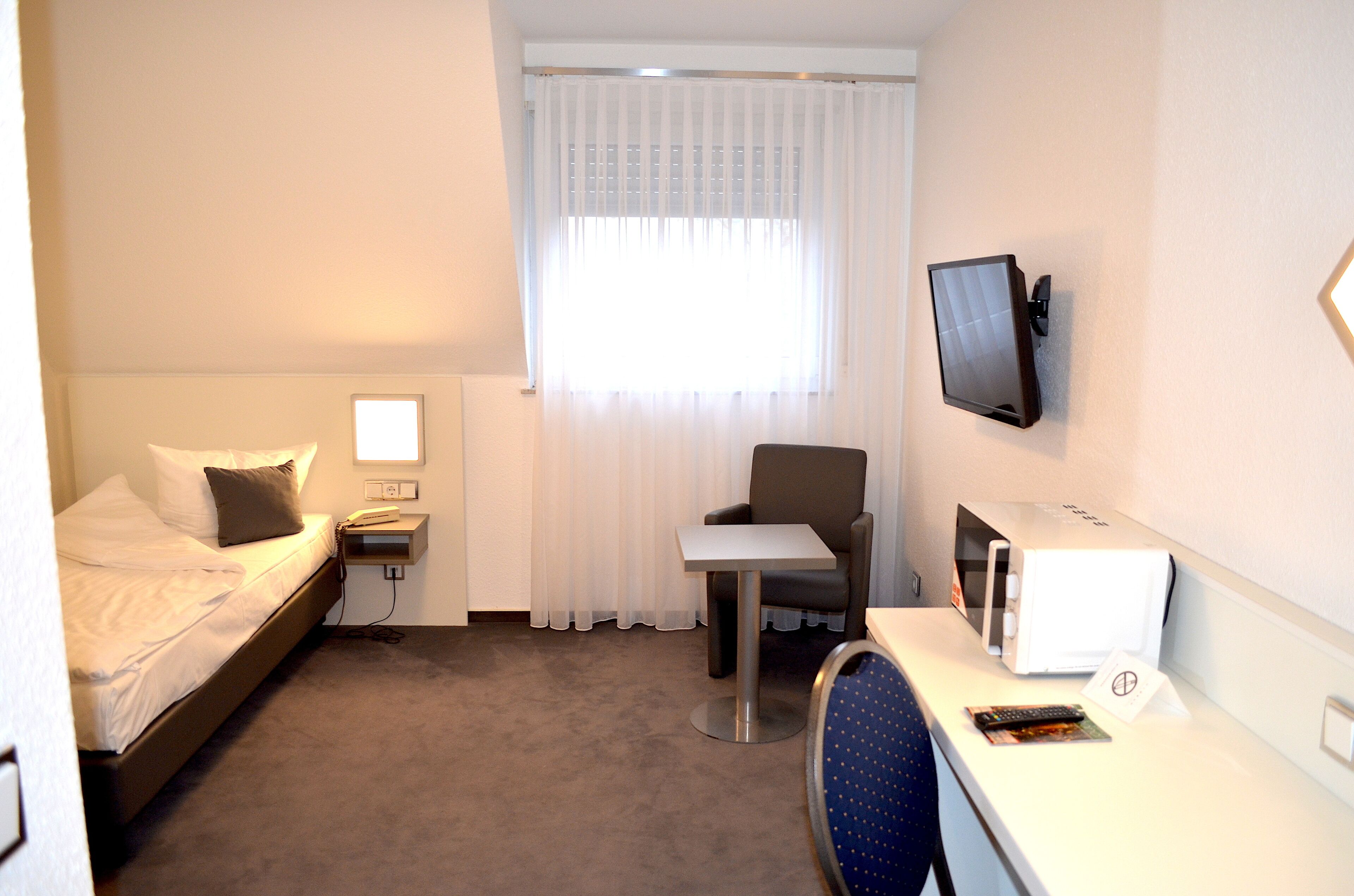 Habitación de hotel con cama, escritorio, silla, televisor y ventana con cortinas.