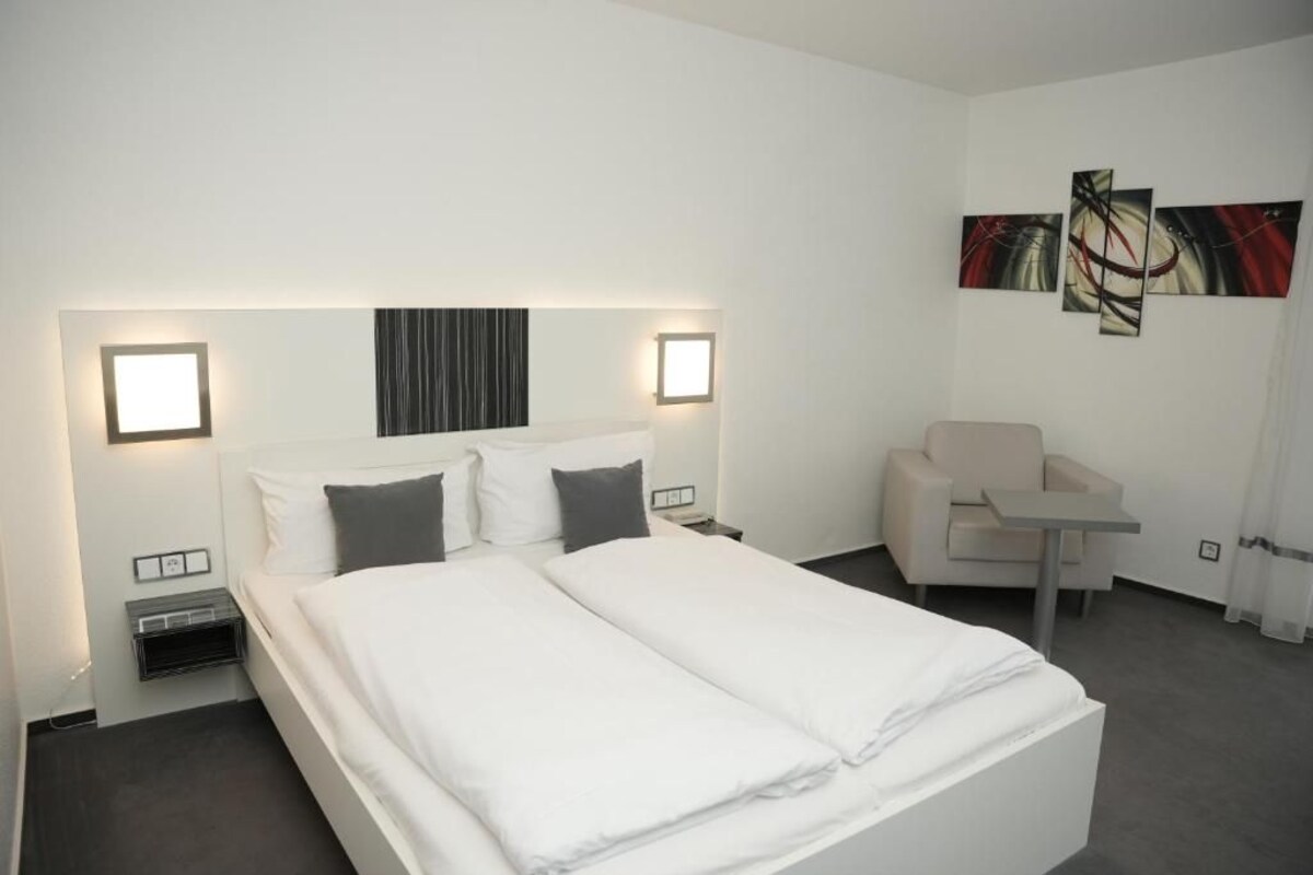 Une chambre d’hôtel avec un lit double, des tables de chevet, une chaise, une petite table et des œuvres d’art abstraites accrochées au mur.