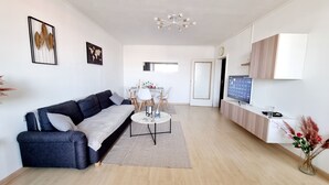 Un salon moderne avec un canapé gris foncé, une table basse ronde et un coin repas comprenant une table et des chaises blanches.