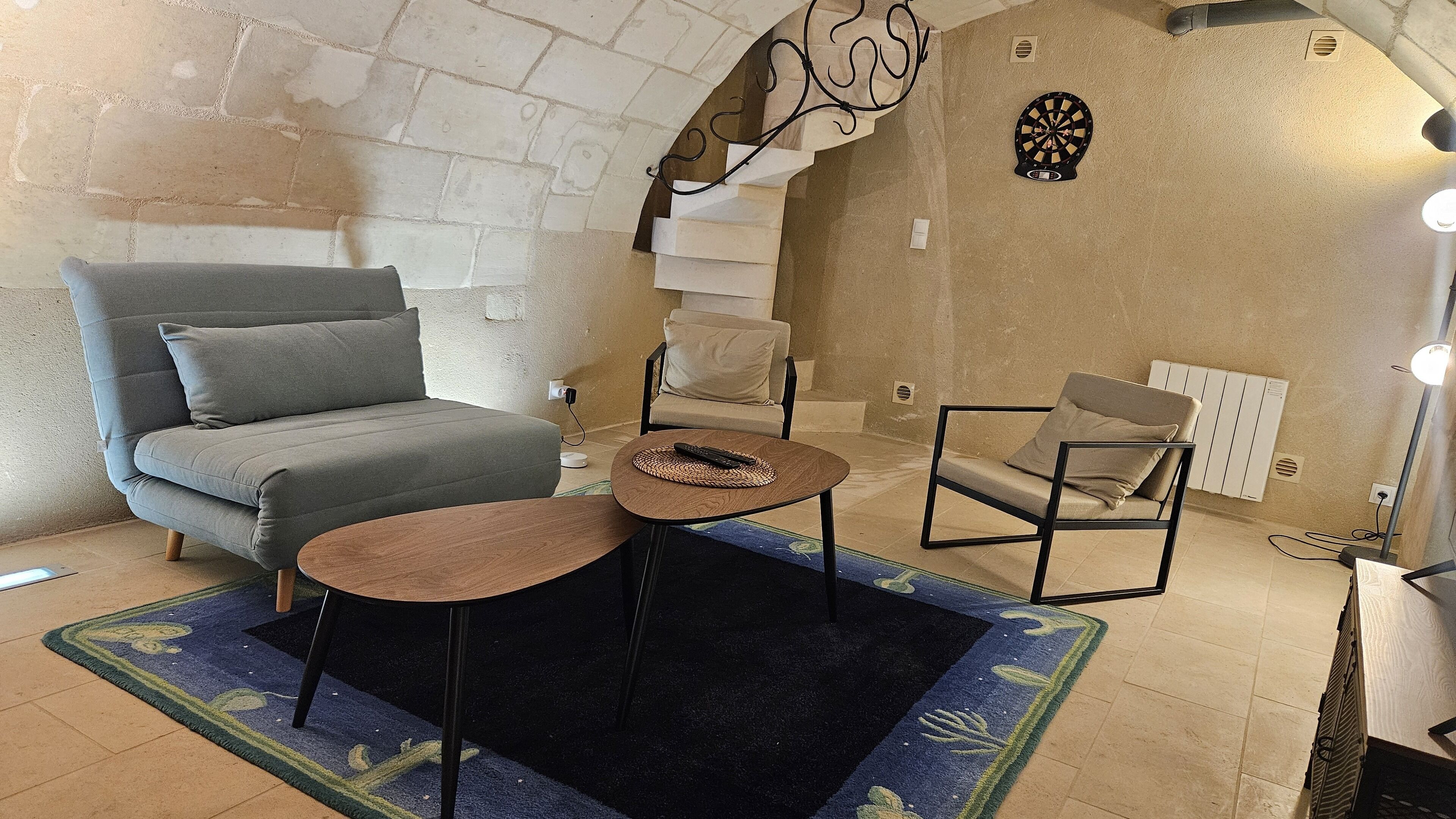 Un salon avec un canapé gris, une petite table ronde, un fauteuil et un élément décoratif mural.