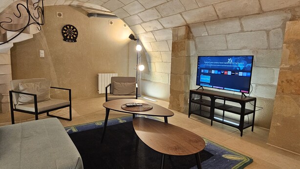Una sala de estar acogedora con pared de piedra, un televisor de pantalla plana, dos sillones, una mesa de centro y una lámpara.