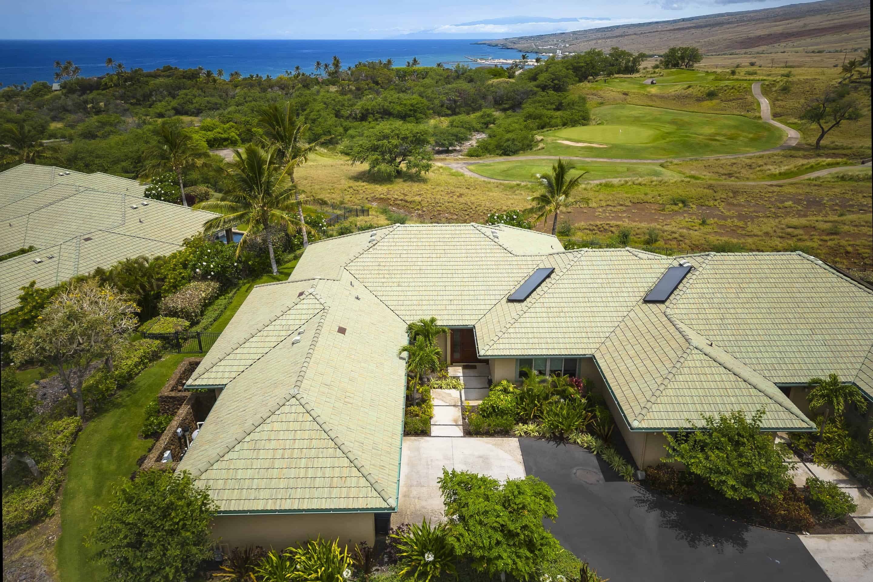 A residential area with multiple houses featuring green roofs and solar panels, surrounded by lush greenery and a golf course.