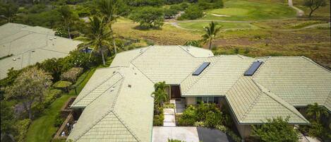 A residential area with multiple houses featuring green roofs and solar panels, surrounded by lush greenery and a golf course.
