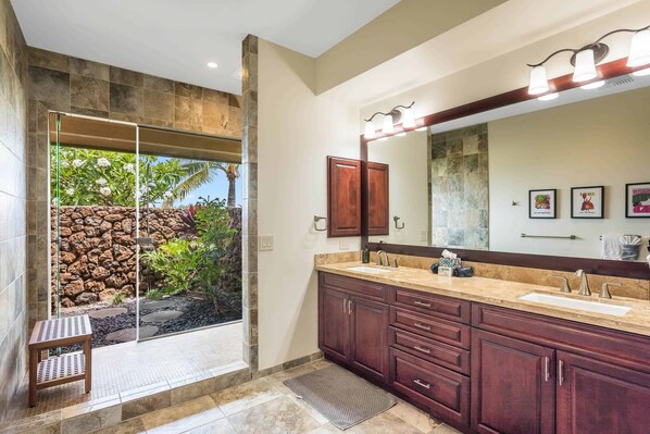 A bathroom with a large mirror, dual sinks, and a stone wall.