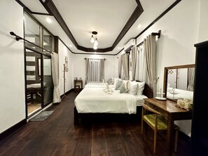 A modern hotel room with a large bed, a wooden desk, and a sliding glass door leading to a balcony. - Aloun Guesthouse (Luang Prabang)
