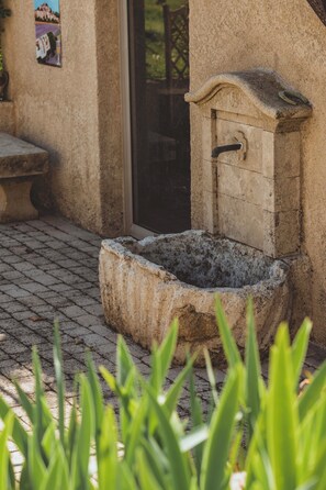 Un pozo de piedra con un caño, una banca y una puerta que da a un área cubierta.