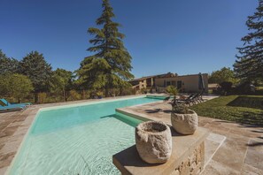 Una piscina con agua cristalina azul, rodeada por una terraza de piedra y plantas en macetas.