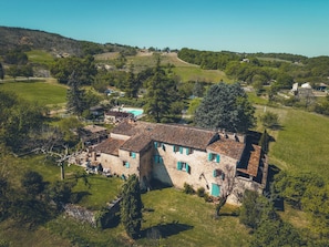 A stone building with a tiled roof, surrounded by greenery and hills.