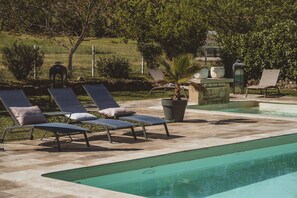 Un área de piscina con sillones de descanso y una palmera.