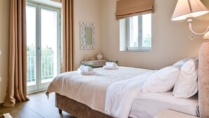 Quarto com cama, janela com cortinas, luminária de cabeceira, espelho e cômoda com toalhas.